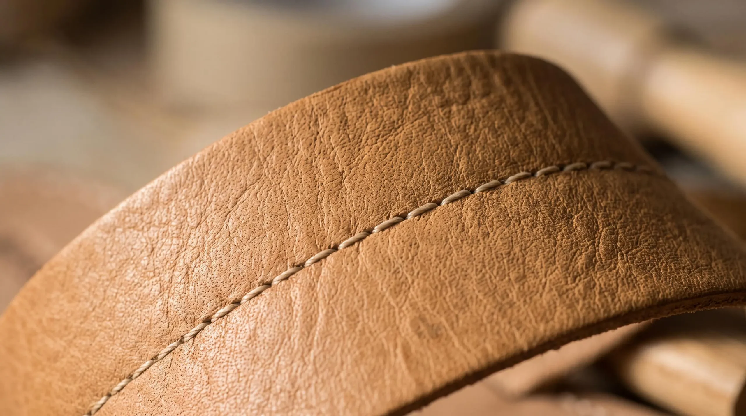 Gros plan macro sur le grain naturel irrégulier d'une bride de sandale en cuir pleine fleur camel, révélant la texture authentique et les pores caractéristiques du matériau noble